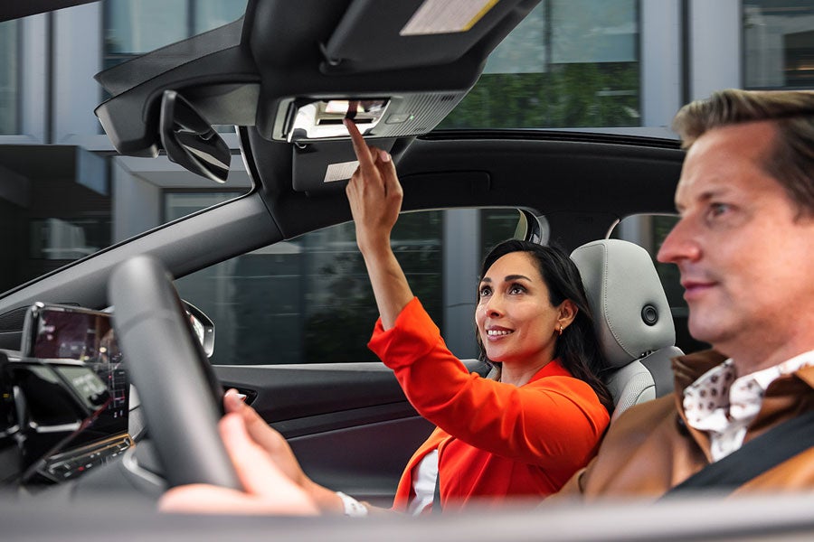 A man and woman sit in the front seats of an ID.4 while the woman in the passenger seat adjusts the controls for the sunshade.