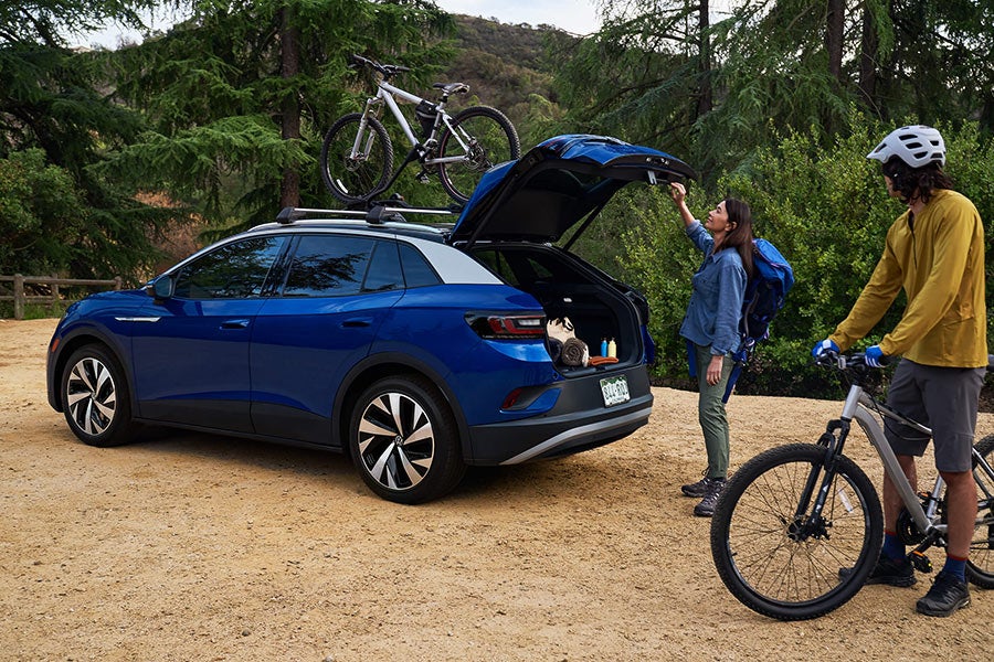 A man and woman load mountain bicycles onto an ID.4 in Dusk Blue Metallic with cross bars and a bike attachment that’s parked in a natural, outdoor setting.