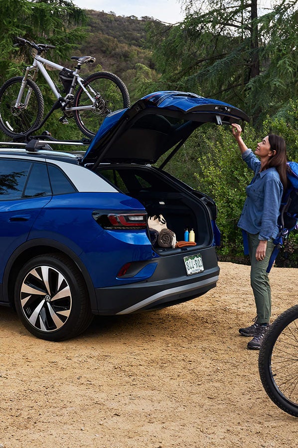 A man and woman load mountain bicycles onto an ID.4 in Dusk Blue Metallic with cross bars and a bike attachment that’s parked in a natural, outdoor setting.