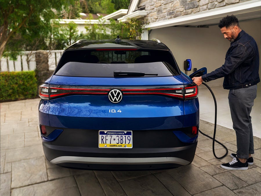 A man charges an ID.4 (in Dusk Blue Metallic) in a residential driveway.