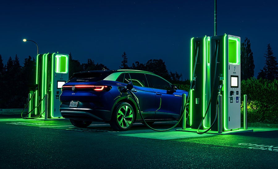 An ID.4 in Dusk Metallic Blue as it is parked at night next to a neon lit charging station.