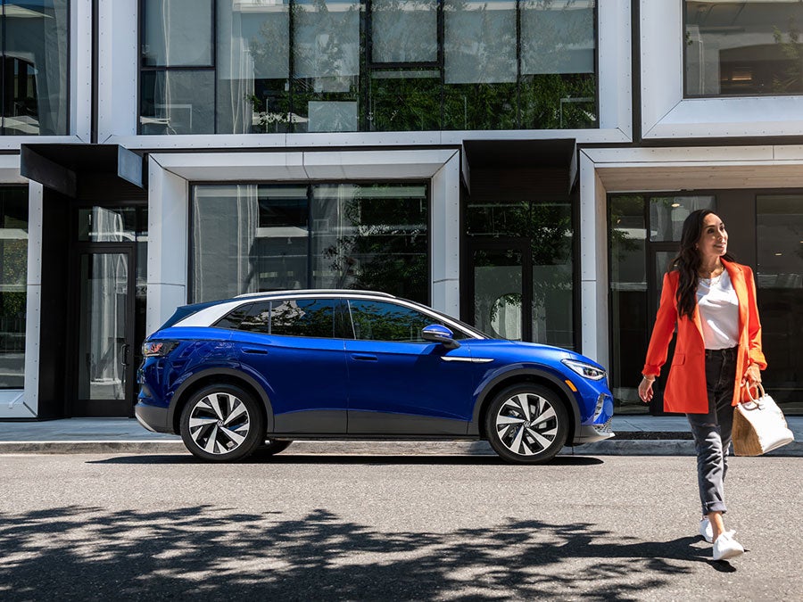 A woman walks away from an ID.4 in Dusk Blue Metallic that’s parked on an urban street.