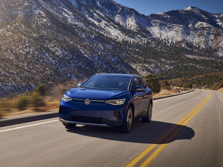 An ID.4 in Dusk Blue Metallic drives along a two-lane highway with mountains in the background.