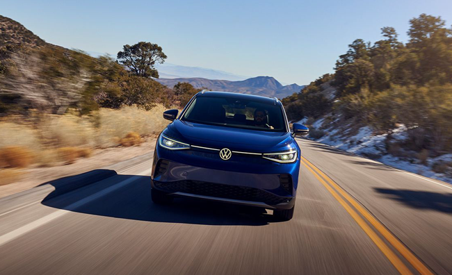 A front shot of an ID.4 in Dusk Blue Metallic cruising down a 2-lane highway in a natural setting.