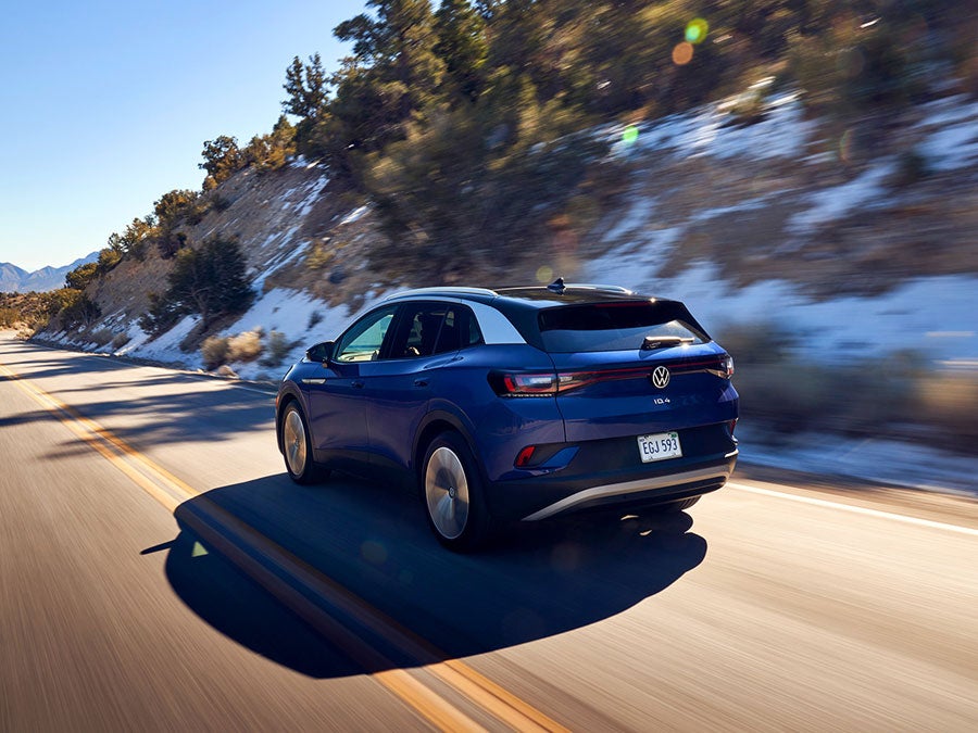 A ¾ rear shot of an ID.4 in Dusk Blue Metallic speeds up a two-lane highway in a mountain setting.